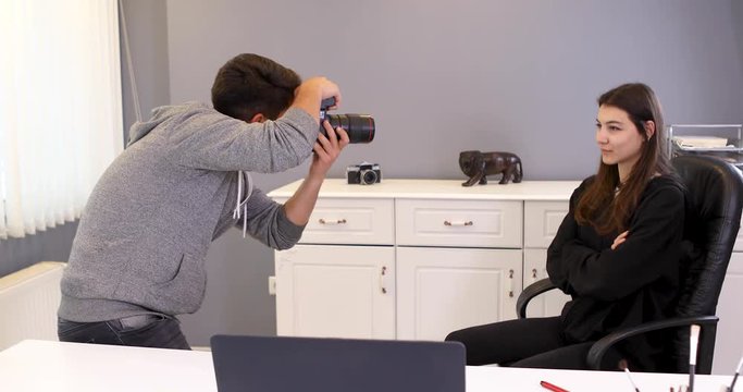 Young woman photographer working in a office taking photos of male model on digital camera