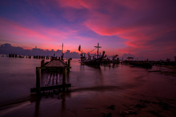 Obraz premium The blurred background of the morning twilight by the sea, changing the color of the beautiful sky, there is a fishing boat docked waiting to go out to find fish again.