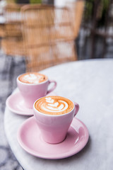 Two pink cups of cappuccino with beautiful latte art on marble table background. Cafe backdrop.