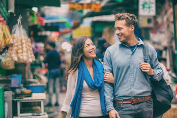 Tourists in Chinatown street market laughing together exploring Asian town. Asia travel adventure, two people walking visiting Hong Kong. Young woman, man in love.