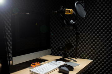 Microphone Condenser, gold mic hang over sound absorbing wall room with wave monitor keyboard mouse game pad controller and headphone in dark audio studio, low exposure lighting background copy space