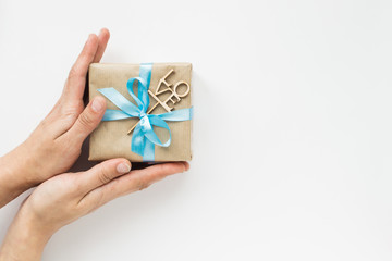 Gift box wrapped in brown paper with blue ribbon in womans hands on white background. Top view. Copyspace