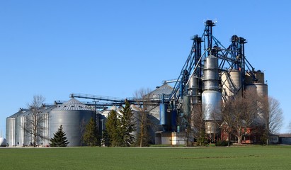 Obraz premium Several grain storage bins and grain dryer with blue sky and grass
