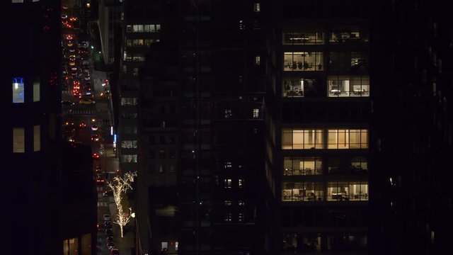 Few offices in a corporate building stay illuminated on a busy night in New York. Scenic view of cars driving around the busy roads winding between lit up skyscrapers in a bustling metropolitan city.