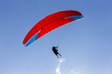 A silhouette of a paraglider with red chute floating across the blue sky