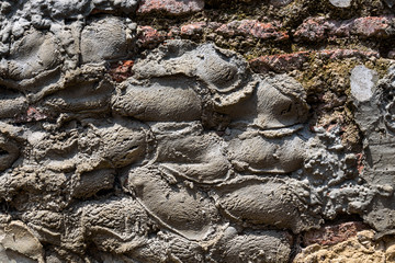 Old weathered masonry wall with crumbling brick and many cement patches, as a textured background