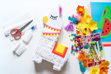 Diy cinco de mayo Mexican Pinata llama made cardboard and crepe paper your own hands on a white background.