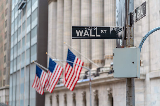 Wall Street "WALL ST" sign over American national flags in front of NYSE stock market exchange building background. The New York Stock Exchange locate in economy district,Business and landmark concept