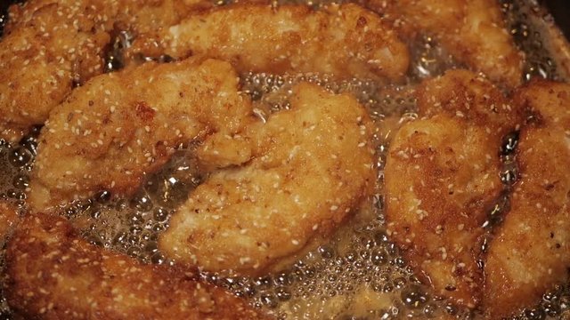 Crumbed breast chicken tenderloins fried in peanut oil in a pan. CLOSE UP. SLOW MOTION.