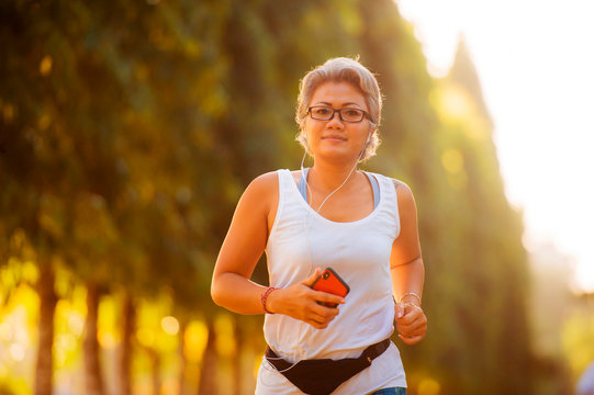 middle aged 40s or 50s happy and attractive woman with grey hair training at city park with green trees on sunrise doing running and jogging workout in health care