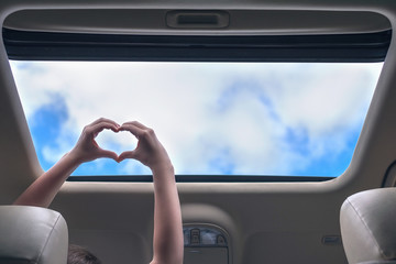 girl traveling by car and holds her hands in the form of heart out from open hatch of a vehicle....