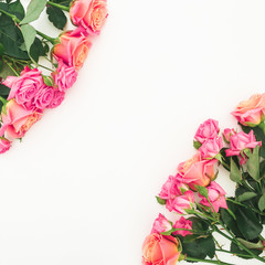 Floral frame of pink flowers and green leaves on white background. Flat lay, top view.