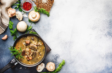 Hot meat vegetable mushroom soup with beef and wholegrain barley. With black bread, in metal pan, top view, gray kitchen table, copy space