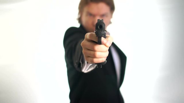 Man aim his gun at the viewer, at youMan in suit un-holsters and aims his gun. A threatening stance, aiming down the sights of his pistol, police, mafia criminal or mercenary. Focus is on the barrel w