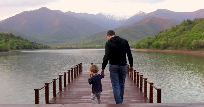 Parent and child go to the pontoon. Father and son walking on lake bridge