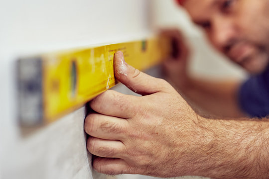 Worker using bubble level for walls and tiles inside the house - renovation fixes.