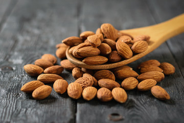 Wooden spoon with scattered almonds on a wooden table.
