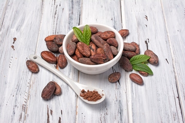 Cocoa beans and powder in white bowl with green leaves