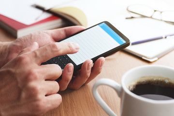 Closeup of male hands touching smartphone screen at table. Smartphone user writing memo.