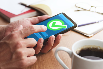Check mark icon on smartphone screen. Closeup of male hands touching smartphone screen at table.