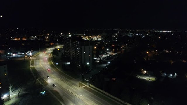 Ascending Aerial Over Downtown City Skyline At Night With Apartment Buildings And Winding Highway Road