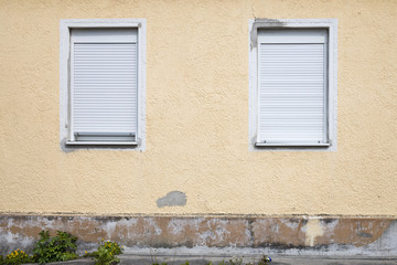 alte, runter gekommene gelbe Hauswand, mit zwei Fenstern, deren Jalousien geschlossen sind