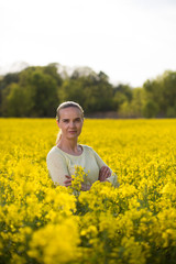 Fototapeta premium Happy woman on blooming rapeseed field in springin yellow blouse.