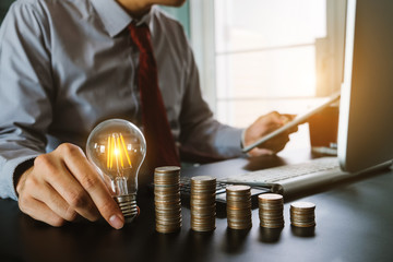 business man hand holding lightbulb with using smartphone and calculator to calculate and money...