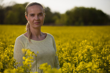 Naklejka na ściany i meble Happy woman on blooming rapeseed field in springin yellow blouse.