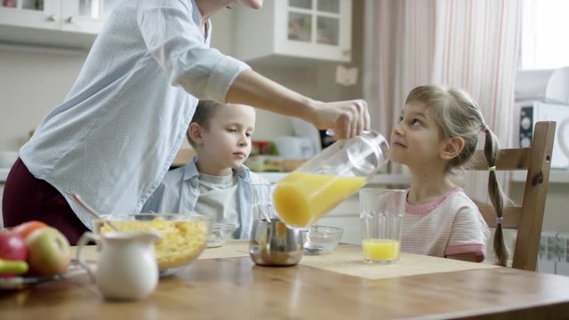 mother communicate during breakfast with her children and add orange juice to cildren's glasses