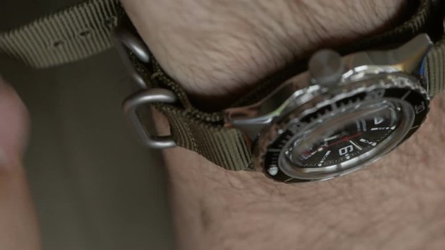 Closeup of the hands of men in khaki clothes, worn on the wrist of the diver's watch on nylon strap.