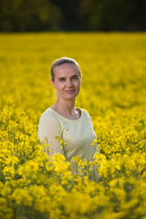 Fototapeta premium Happy woman on blooming rapeseed field in springin yellow blouse.