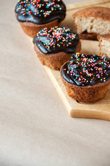 On the table fresh cupcakes drenched with chocolate and decorative sprinkles diagonally on a wooden Board.