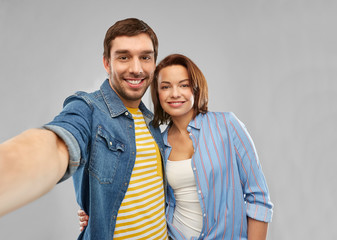 Naklejka premium people concept - happy couple hugging and taking selfie over grey background