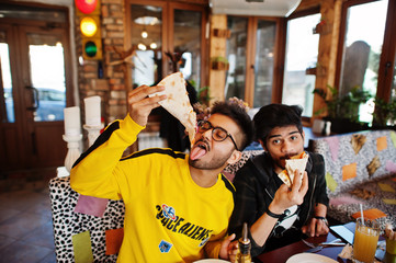 Asian friends guys eating pizza during party at pizzeria. Happy indian people having fun together, eating italian food and sitting on couch.