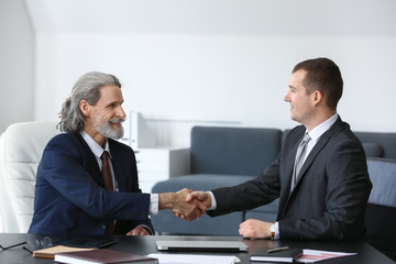 Mature businessman shaking hands with young colleague in office