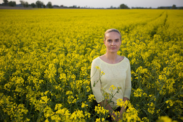 Fototapeta premium Happy woman on blooming rapeseed field in springin yellow blouse.