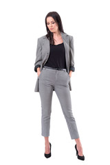 Serious fashion woman in business suit clothes looking down with hands in pockets. Full body isolated on white background.