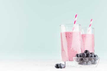 Fresh violet cocktail with blueberries in bowl, striped straw on pastel mint color background and white wood table, copy space.