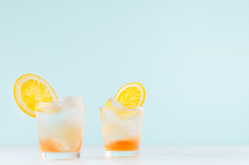 Summer fresh alcoholic drinks with oranges liquor, ice cubes in shot glass on blue wall, copy space.