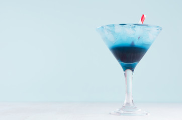 Sweet summer cold alcohol blue drink with ice cubes, red straw in  wineglass on soft light pastel blue background.