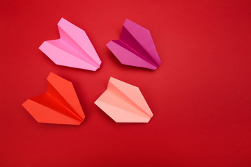 Flat lay of colour paper planes on red background with text space.