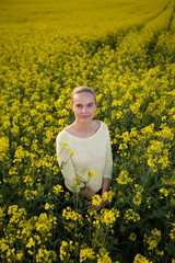 Fototapeta premium Happy woman on blooming rapeseed field in springin yellow blouse.