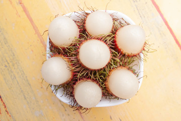 Rambutan fruits in white bowl has a delicious sweet taste on old yellow cement table background.
