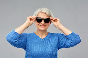 valentine's day, summer and old people concept - portrait of smiling senior woman in red black sunglasses over grey background