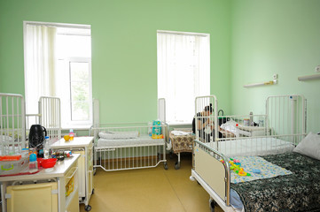 Interior of a hospital room. Woman sitting on a bed of a hospital room, baby laying in a bed