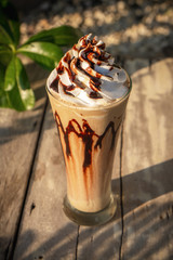 Coffee frappe with whipped cream on old wooden table in the morning sun.