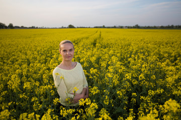 Fototapeta premium Happy woman on blooming rapeseed field in springin yellow blouse.