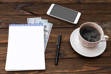 Notebook, us dollar bills, smartphone, pen, Cup of coffee on wooden background. business planning.