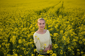 Fototapeta premium Happy woman on blooming rapeseed field in springin yellow blouse.